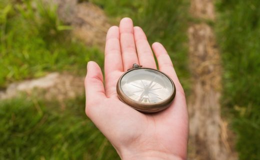 Hand holding old fashioned compass showing the way on a country trail